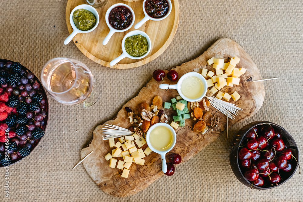 Various cheeses on a wooden board, with honey, pesto, berries and fruits. Summer picnic concept.