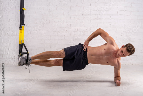 Muscular young man doing exercises with trx straps, near a white brick wall. photo