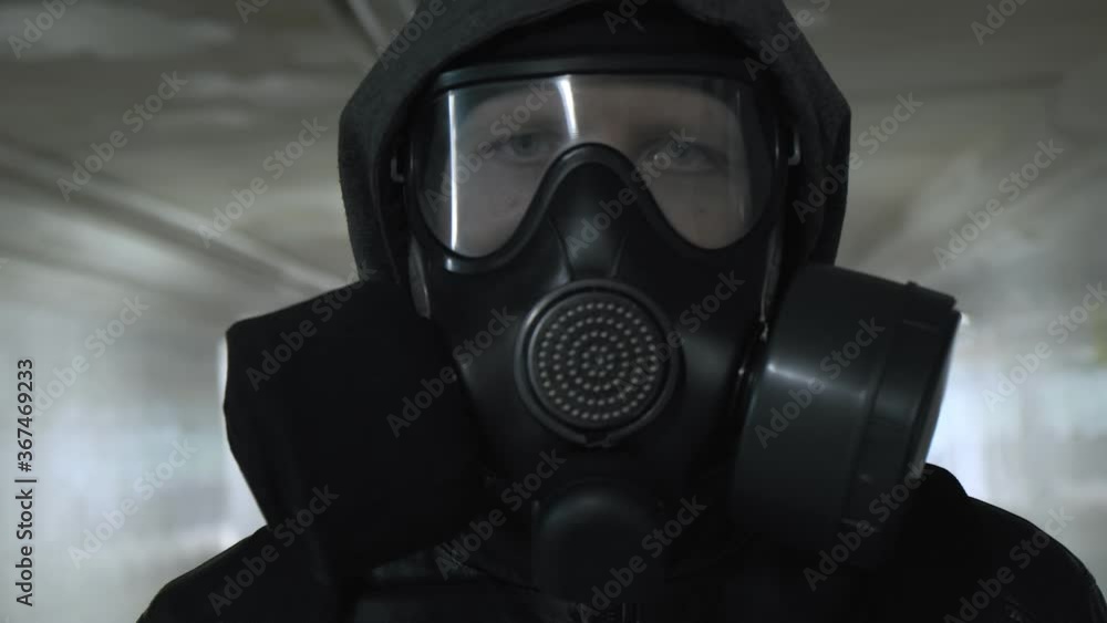 man in gas mask, black jacket with hood walking through long tunnel, underpass. protection from chemical weapons, virus epidemic. Post apocalyptic world. survivor, stalker after nuclear, chemical war man in gas mask, black jacket with hood walking through long tunnel, underpass. protection from chemical weapons, virus epidemic. Post apocalyptic world. survivor, stalker after nuclear, chemical war