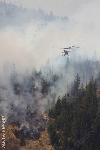 Forest fire. Firefighting helicopter lowers water under fire of helicopter and extinguishes huge forest fires.  Special helicopter in flight  suspension with a fire extinguishing drainage device