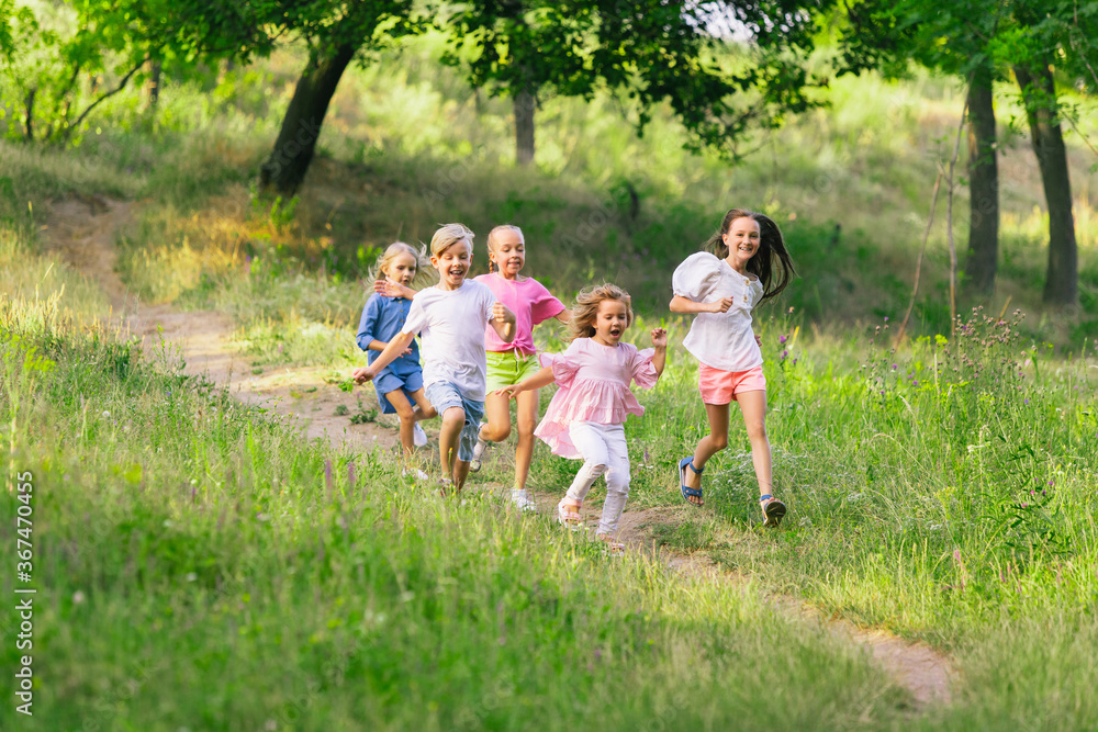 Kids, children running on meadow in summer's sunlight. Look happy, cheerful with sincere bright emotions. Cute caucasian boys and girls. Concept of childhood, happiness, movement, family and summer.