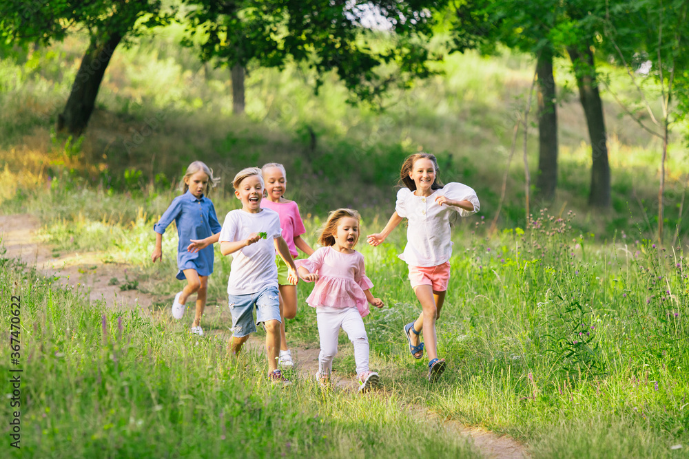 Naklejka premium Kids, children running on meadow in summer's sunlight. Look happy, cheerful with sincere bright emotions. Cute caucasian boys and girls. Concept of childhood, happiness, movement, family and summer.