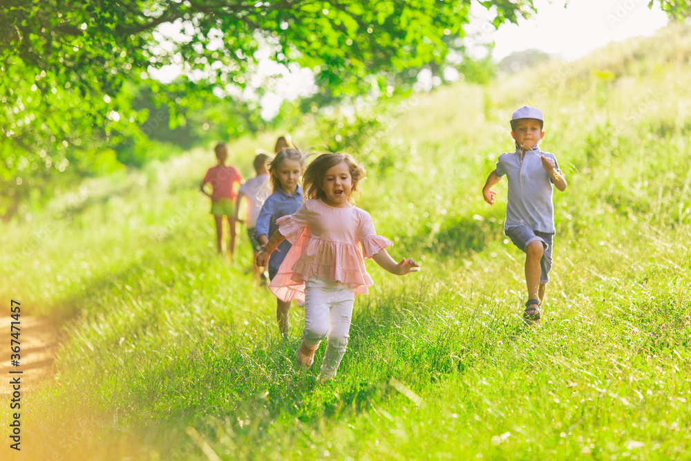 Kids, children running on meadow in summer's sunlight. Look happy, cheerful with sincere bright emotions. Cute caucasian boys and girls. Concept of childhood, happiness, movement, family and summer.