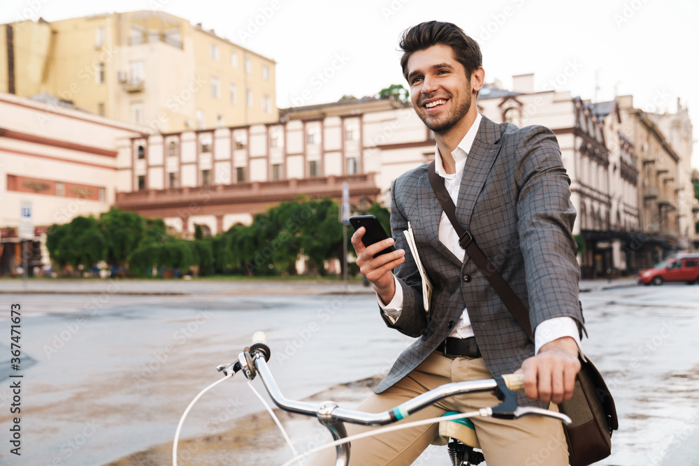 Image of happy businessman smiling and using cellphone on bicycle Image of happy businessman smiling and using cellphone on bicycle