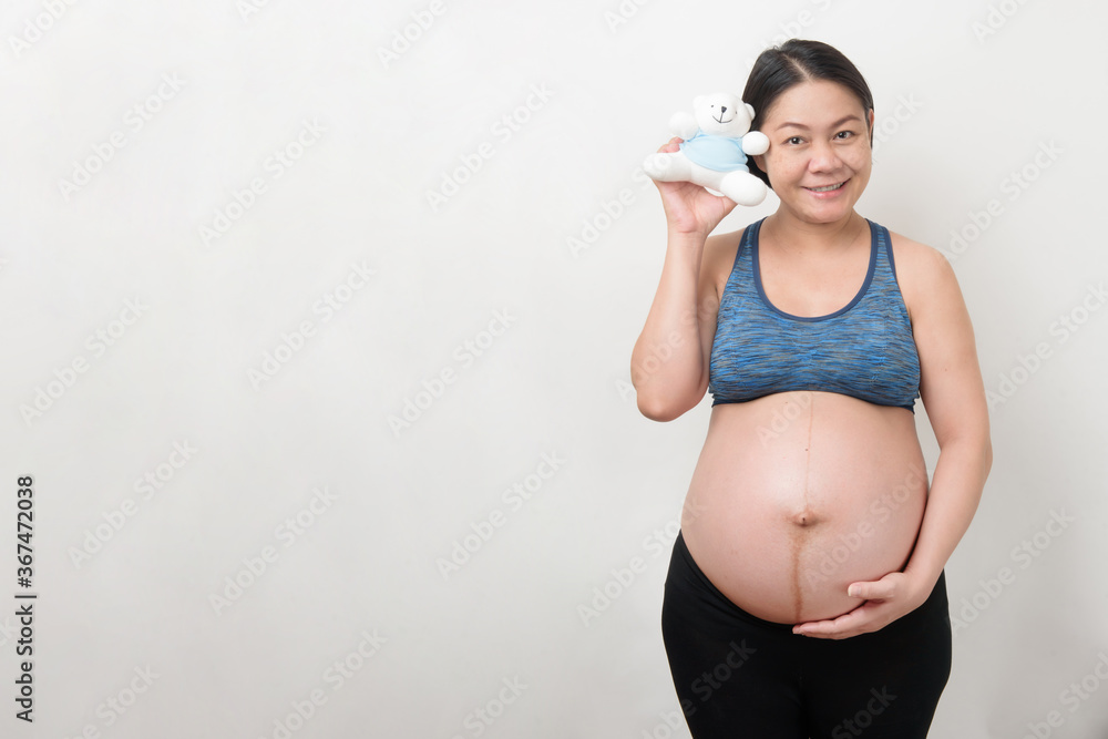 Happy Asian pregnant mother in the smiley face holding and show the little blue teddy bear, isolated on white background, pregnancy concept.. Happy Asian pregnant mother in the smiley face holding and show the little blue teddy bear, isolated on white background, pregnancy concept..