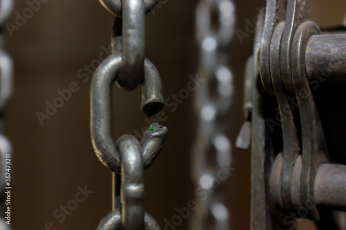 Broken chain link of a manual winch in an old factory building. Dark background. Blurred frame. Selective focus