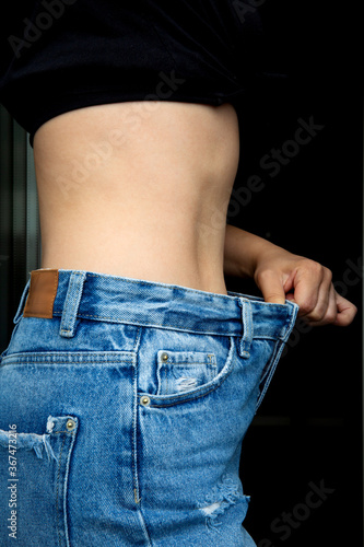 Fototapeta Naklejka Na Ścianę i Meble -  Slimming concept. The girl holds jeans in her hand, shows a thin waist Slim female body in large jeans. Diet concept. 