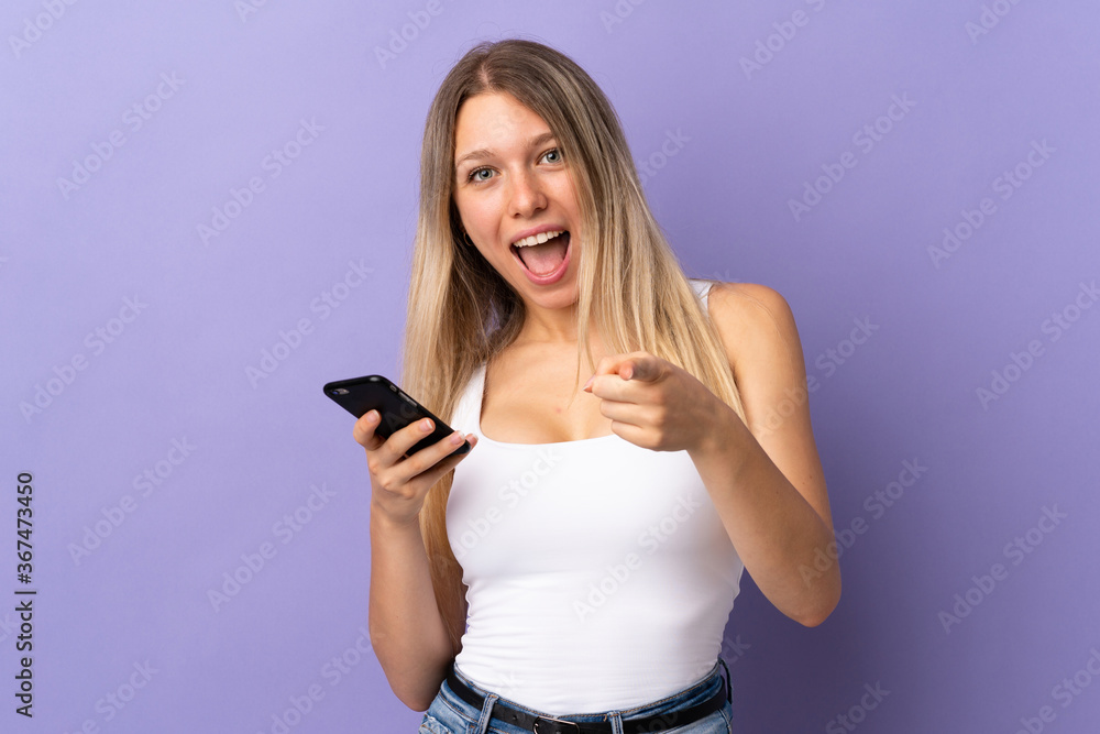 Young blonde woman using mobile phone isolated on purple background points finger at you Young blonde woman using mobile phone isolated on purple background points finger at you