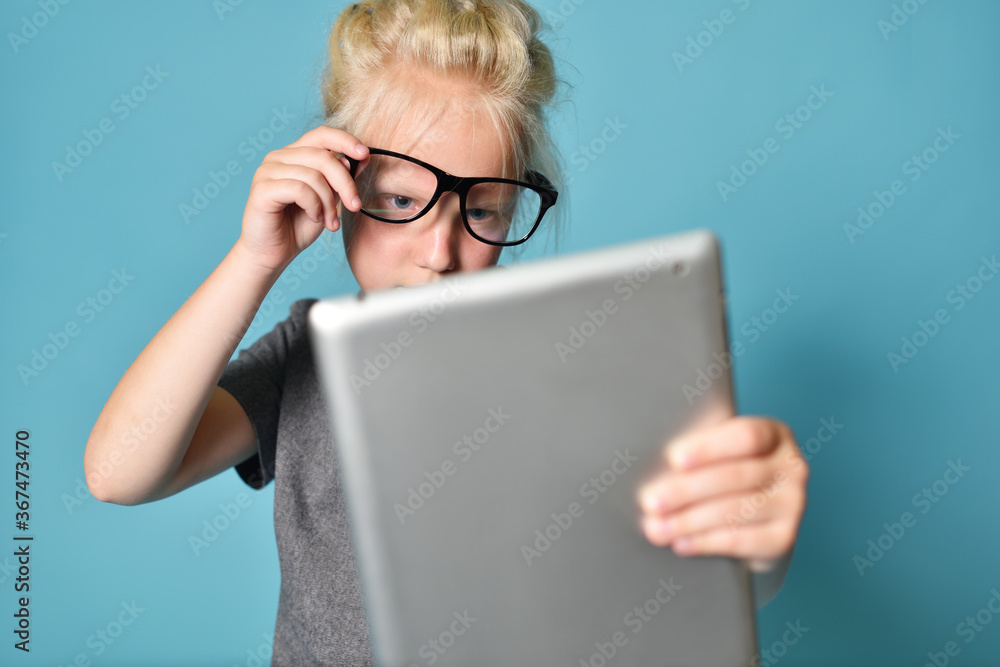 Girl child in glasses, plays on a tablet computer and strains eyesight Girl child in glasses, plays on a tablet computer and strains eyesight