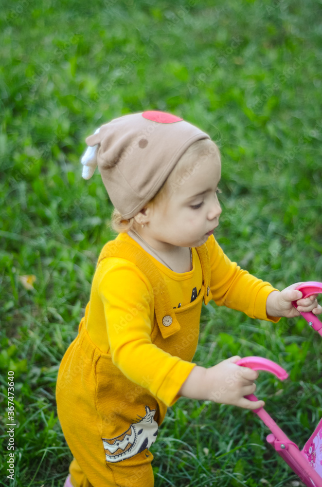Photo of a toddler girl in the funny hat playing with a toy stroller Photo of a toddler girl in the funny hat playing with a toy stroller