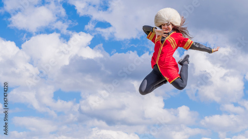 A young girl is dancing in the clouds and jumping in a national Caucasian costume (lezginka) and in a white hat. Summer Adventures.