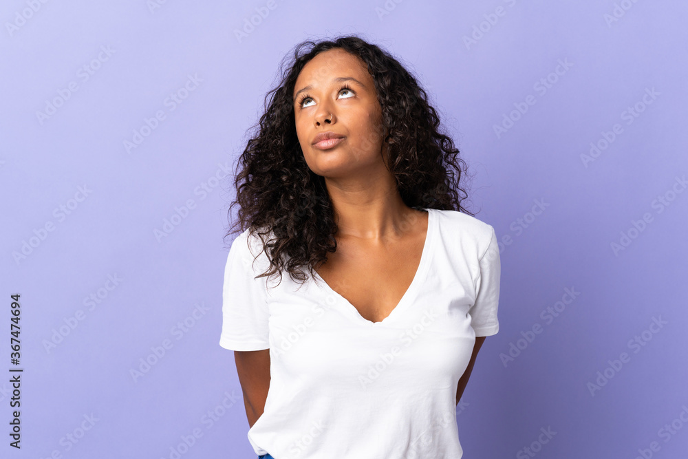 Teenager cuban girl isolated on purple background and looking up Teenager cuban girl isolated on purple background and looking up