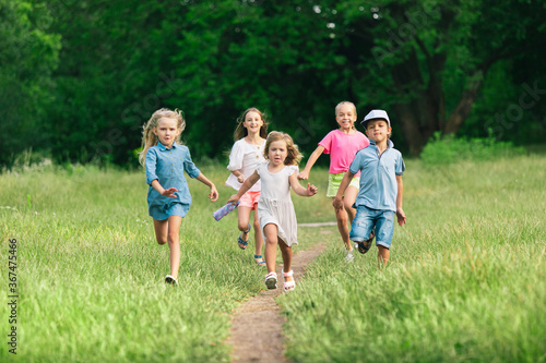 Kids  children running on meadow in summer s sunlight. Look happy  cheerful with sincere bright emotions. Cute caucasian boys and girls. Concept of childhood  happiness  movement  family and summer.