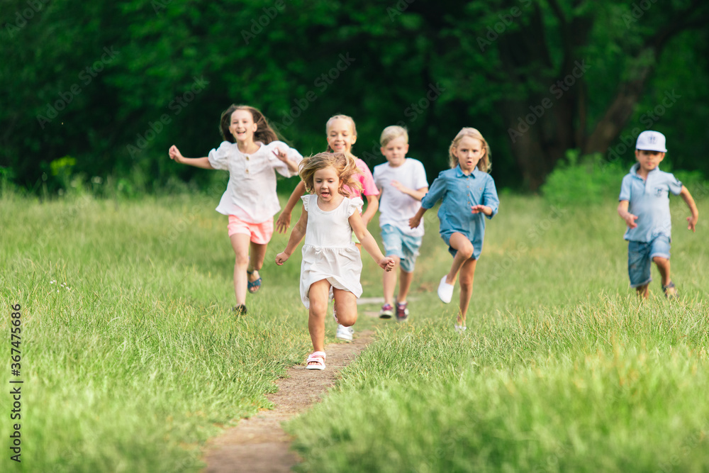 Kids, children running on meadow in summer's sunlight. Look happy, cheerful with sincere bright emotions. Cute caucasian boys and girls. Concept of childhood, happiness, movement, family and summer. Kids, children running on meadow in summer's sunlight. Look happy, cheerful with sincere bright emotions. Cute caucasian boys and girls. Concept of childhood, happiness, movement, family and summer.