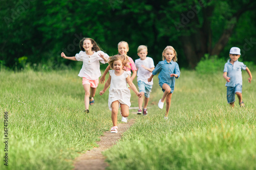 Kids, children running on meadow in summer's sunlight. Look happy, cheerful with sincere bright emotions. Cute caucasian boys and girls. Concept of childhood, happiness, movement, family and summer. © master1305