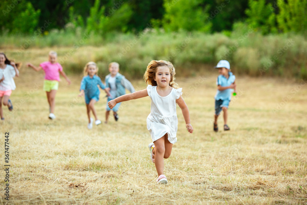 Kids, children running on meadow in summer's sunlight. Look happy, cheerful with sincere bright emotions. Cute caucasian boys and girls. Concept of childhood, happiness, movement, family and summer. Kids, children running on meadow in summer's sunlight. Look happy, cheerful with sincere bright emotions. Cute caucasian boys and girls. Concept of childhood, happiness, movement, family and summer.