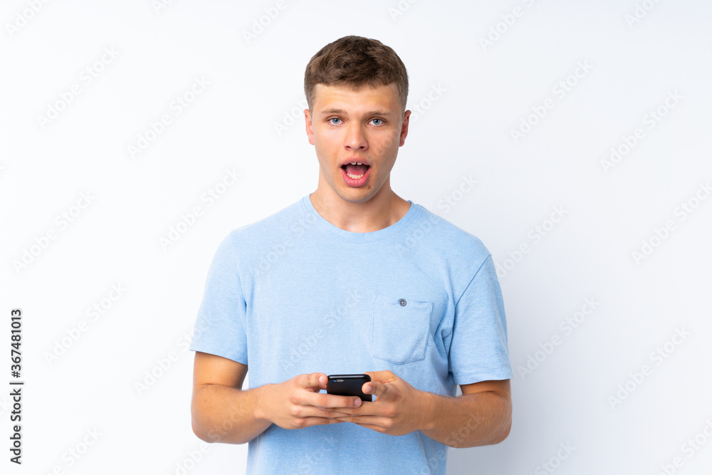 Young handsome man over isolated white background surprised and sending a message Young handsome man over isolated white background surprised and sending a message