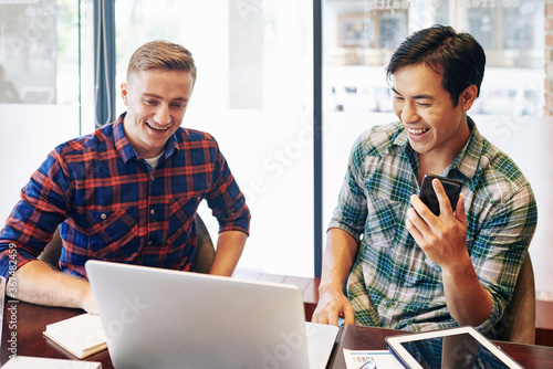 Cheerful multi-ethnic young people watching funny video on laptop during break in office
