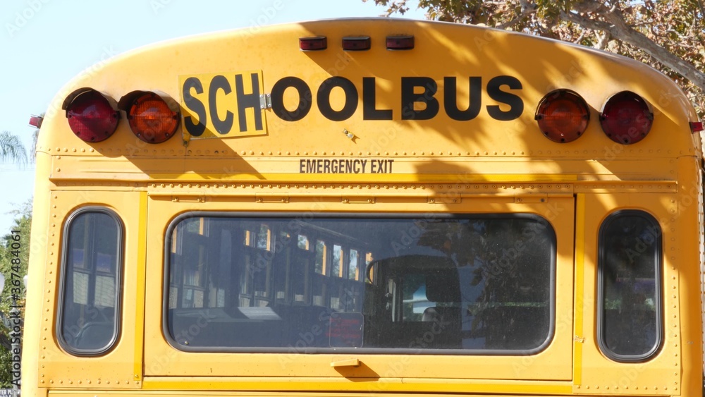Yellow iconic school bus in Los Angeles, California USA. Classic truck for students back view. Vehicle stoplights for safety of children transportation. Public passenger transport for kids in suburb