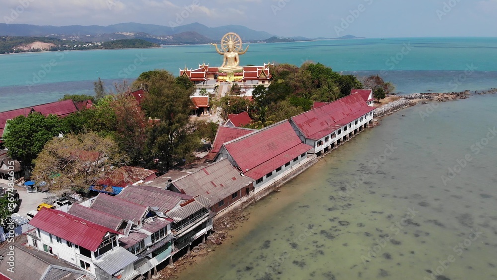 Island with Buddhist temple and many houses. Aerial view of island with Buddhist temple with statue Big Buddha surrounded by traditional houses on stilts in bay of Pacific ocean on Samui, Thailand.