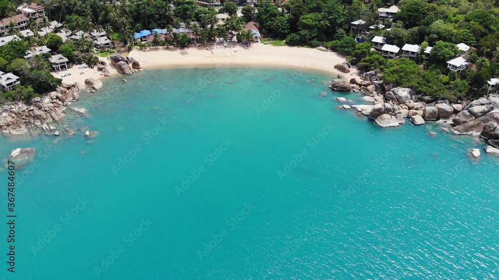 Small houses on tropical island. Tiny cozy bungalows located on shore of Koh Samui Island near calm sea on sunny day in Thailand. Volcanic rocks and cliffs drone top view.