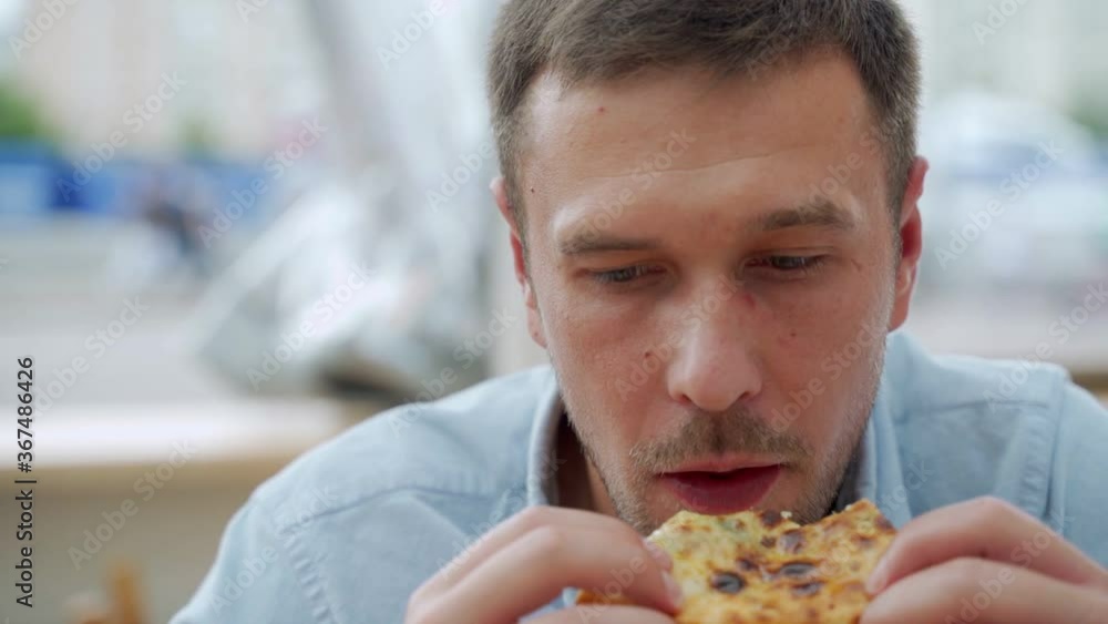 Handsome young man eating a slice of pizza outside on the street Handsome young man eating a slice of pizza outside on the street