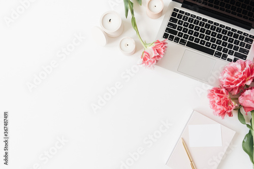 Laptop and beautiful pink peony tulip flowers, blank paper sheet card, candles on white background. Flat lay, top view minimalist home office desk workspace with blank copy space