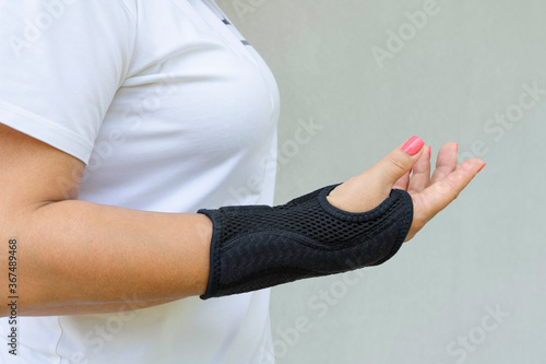 Black wrist brace or corset is worn on women's hand for treatment of carpal tunnel syndrome or median nerve compression, numbness hand photo