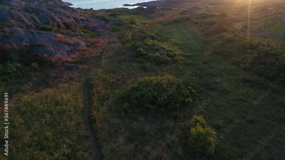 An aerial shot following a path going through high grass and ending up in a rocky bay during a sunset. An aerial shot following a path going through high grass and ending up in a rocky bay during a sunset.