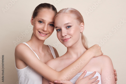 Beauty Models Portrait. Cheerful girls stick their hands together and laugh. Girls with natural makeup stand together on a beige background