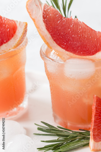Grapefruit lemonade. Two cold wet drinking glasses with fresh grapefruit nonalcohol beverage. Ice, rosemary.