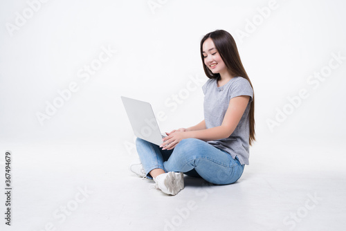 Young woman sitting on the floor with laptop isolated on white background © dianagrytsku