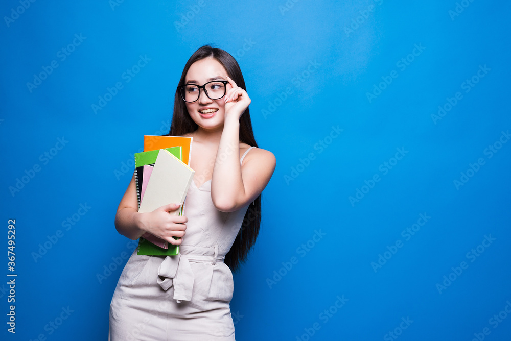 Young asian woman smiles and holds books in her hands on a blue background. Concept of education, college, session, exam. Young asian woman smiles and holds books in her hands on a blue background. Concept of education, college, session, exam.