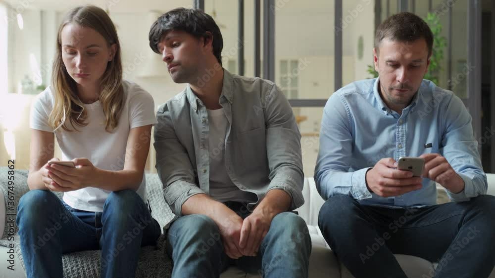 Bored man sitting on couch between gadget addicted friends with smartphones Bored man sitting on couch between gadget addicted friends with smartphones
