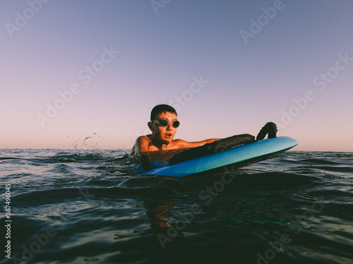 A young boy playing with a body table  in the water in the sunset time in summer © Dellealpi