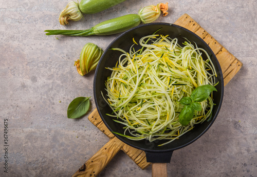 Zucchini vegetable noodles - green zoodles or courgette spaghetti on plate over gray background. Clean eating, raw vegetarian food concept. Copy space for text. Top view or flat lay