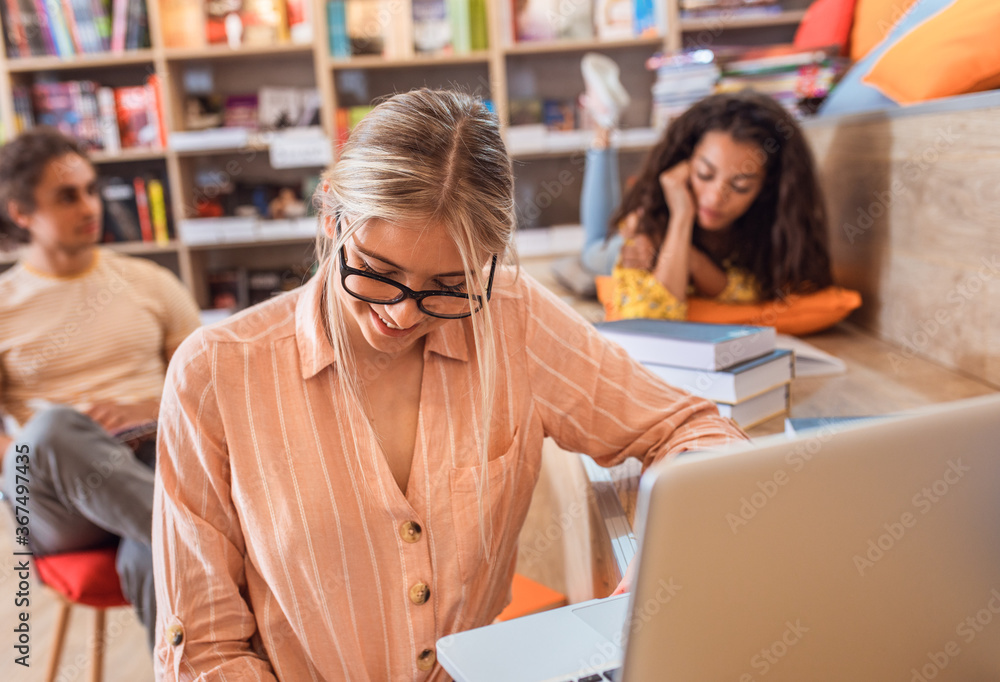 Portrait of young female student study in the library using laptop for researching online with friends in background. Portrait of young female student study in the library using laptop for researching online with friends in background.