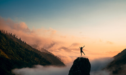 Silhouette of a Man jump and rises arms up on a peak. The happiness and excitement of beeing successful.