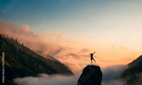 Fotografia Silhouette of a Man jump and rises arms up on a peak