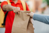 Give order to client in town. Deliveryman in uniform with yellow backpack holds paper bag