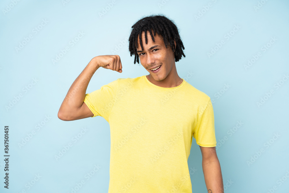 Young african american man isolated on blue background doing strong gesture Young african american man isolated on blue background doing strong gesture