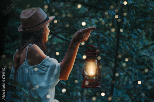 Beautiful woman in white dress holding a lantern in a forest with blurred glowings under the trees. photo