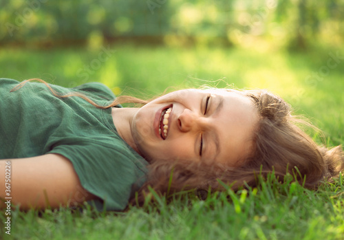 Happy laughing fun casual kid girl lying on the grass on nature summer background. Closeup positive