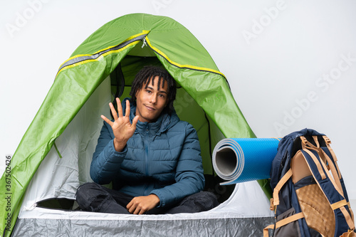 Young african american man inside a camping green tent counting five with fingers