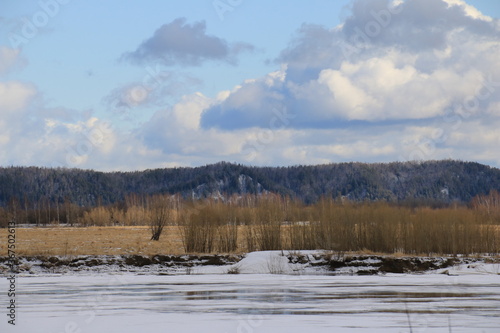 Spring in the North. Ice-covered river, snowy expanses, yellowed bushes and hills on the horizon © Илья Юрукин