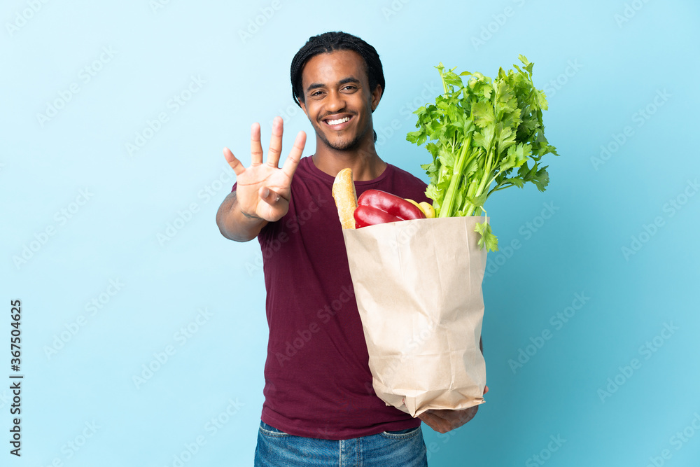 African American man holding a grocery shopping bag isolated on blue background happy and counting four with fingers African American man holding a grocery shopping bag isolated on blue background happy and counting four with fingers
