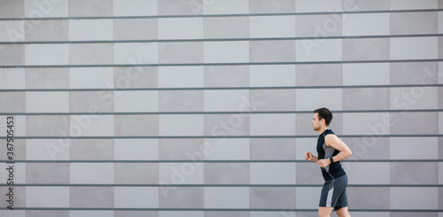 Jogging in city. Slender guy in sportswear with fitness tracker  runs