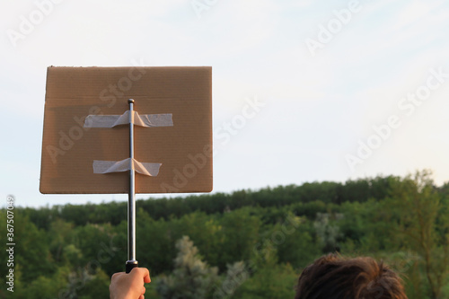 Man walkst hrough the park to protest. In his hand he holds a periscopic baton to which a cardboard plaque is attached photo