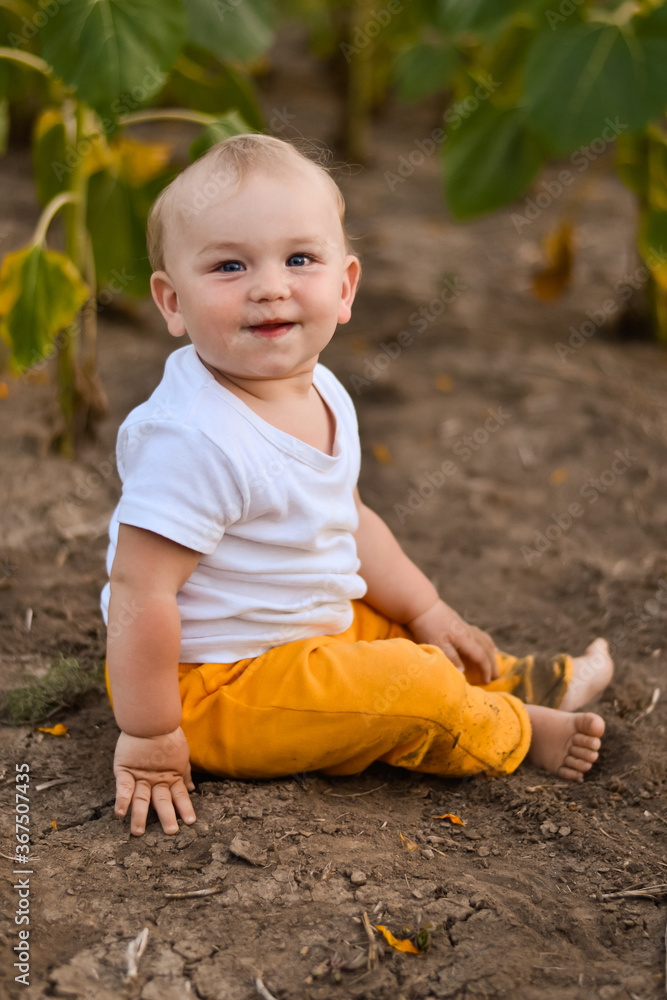 a happy baby sits on the ground in a field and smiles