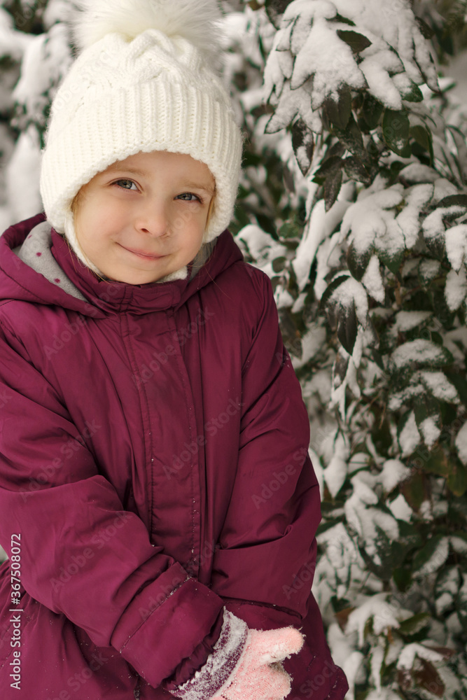 Portrait of a little cute emotional girl on a background of a snowy Christmas tree. Walk on a winter snowy day. Happy childhood. Games, freedom and carefree Portrait of a little cute emotional girl on a background of a snowy Christmas tree. Walk on a winter snowy day. Happy childhood. Games, freedom and carefree